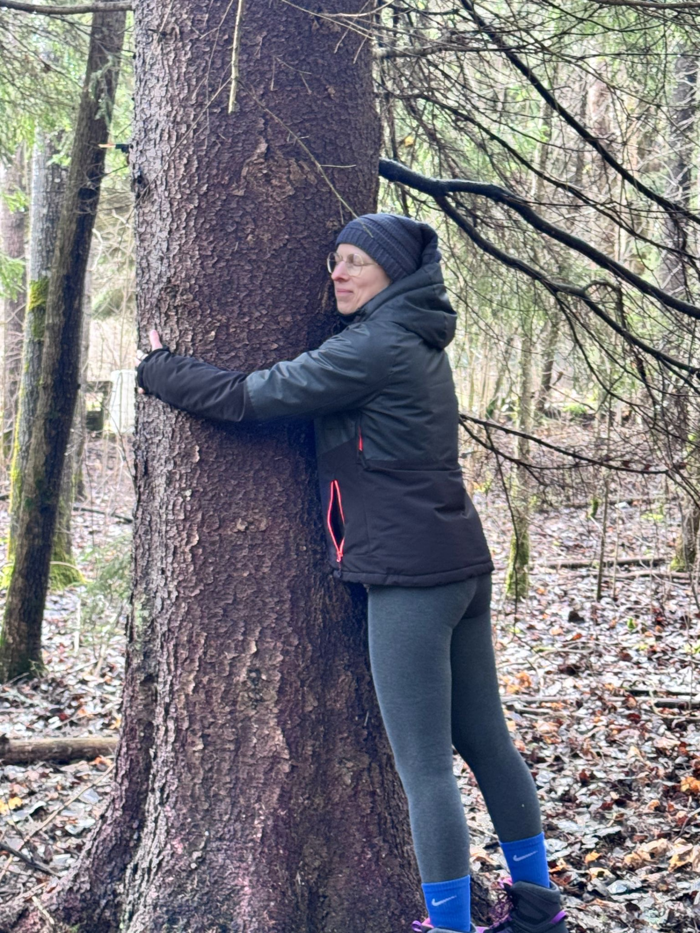 A woman holding on to a spruce trunk in a bare winter forest